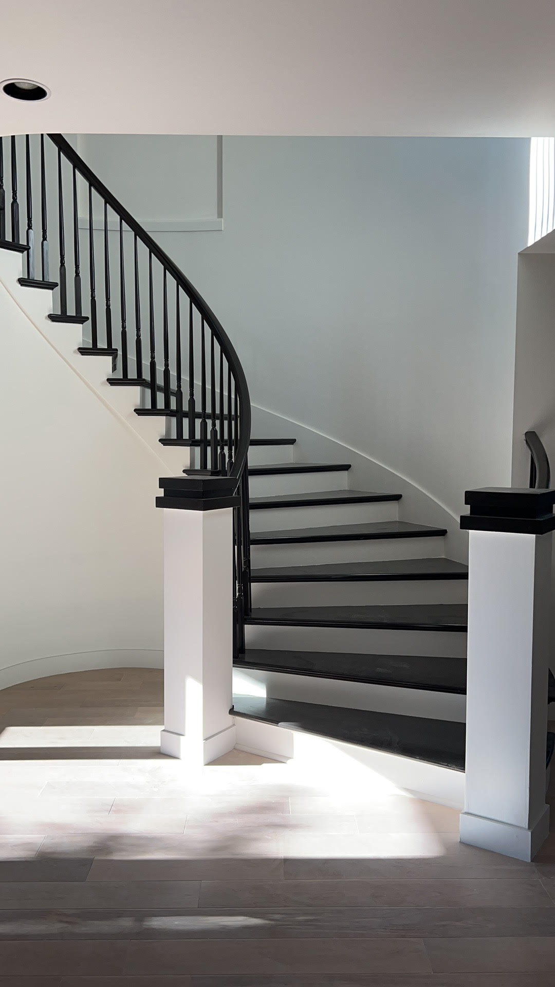Elegant curved staircase with black treads and iron balusters in a whole home remodel